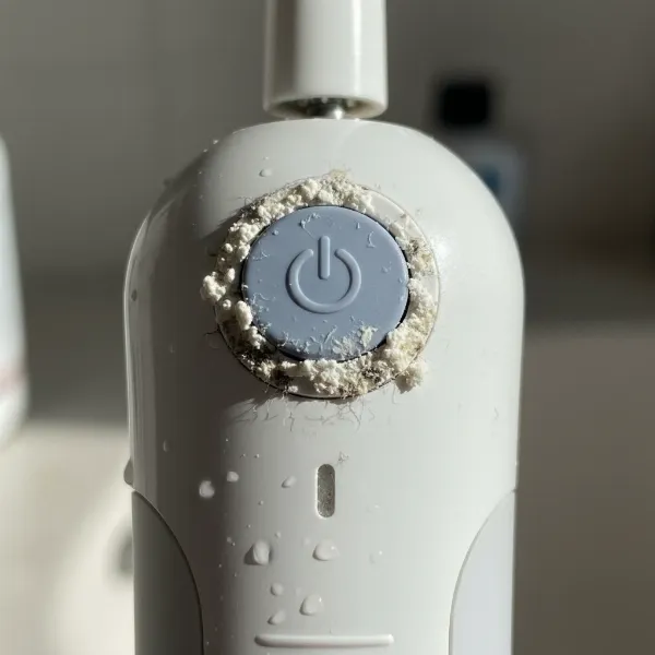 Close-up of electric toothbrush power button with toothpaste residue and grime around it